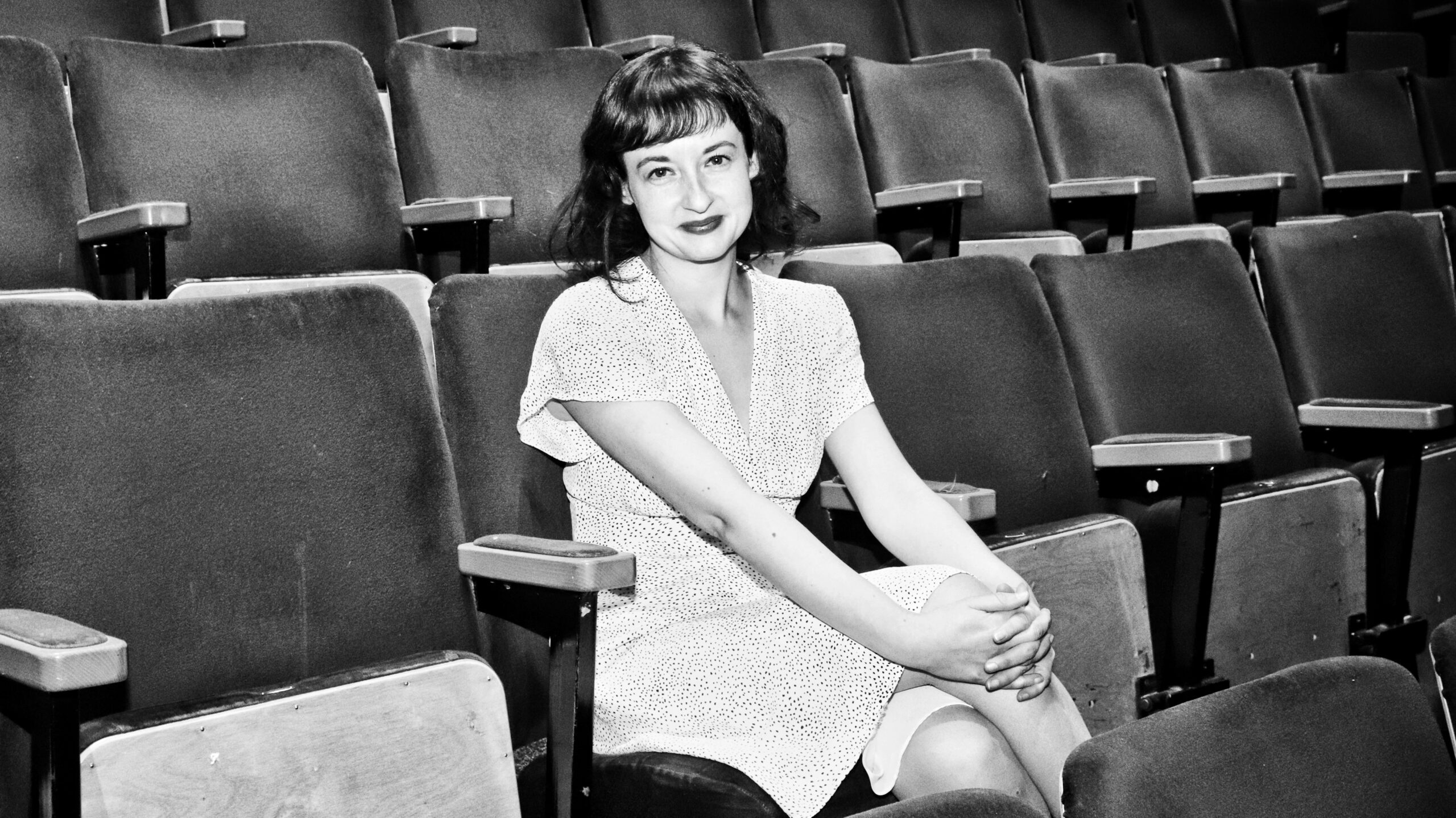 A picture of Chloe Wade, writer of As She Likes it, in black and white, as she sits in a theatre